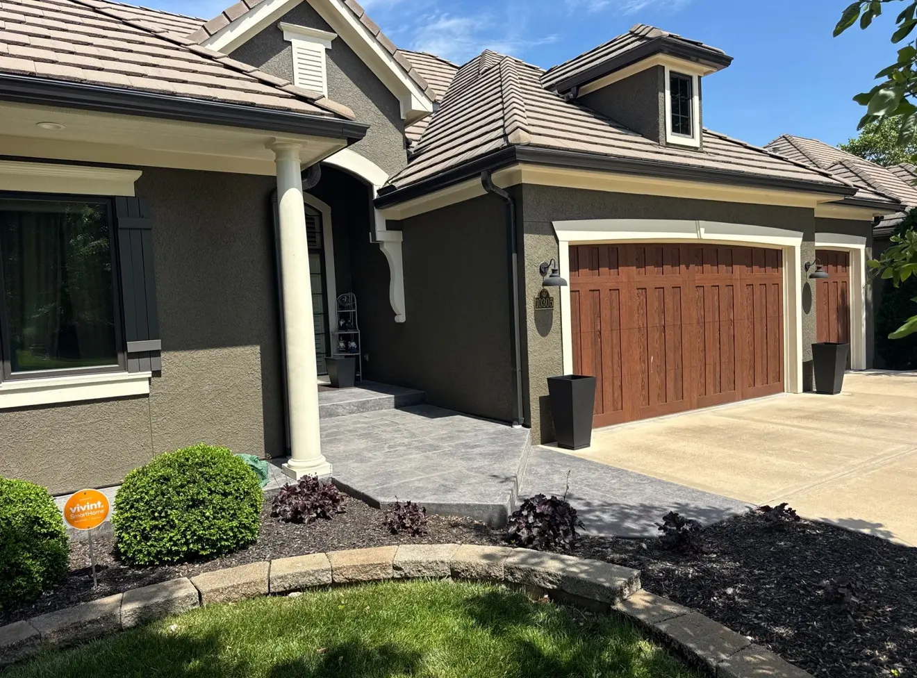 Freshly painted stucco exterior with stained wood-look garage doors and crisp white trim