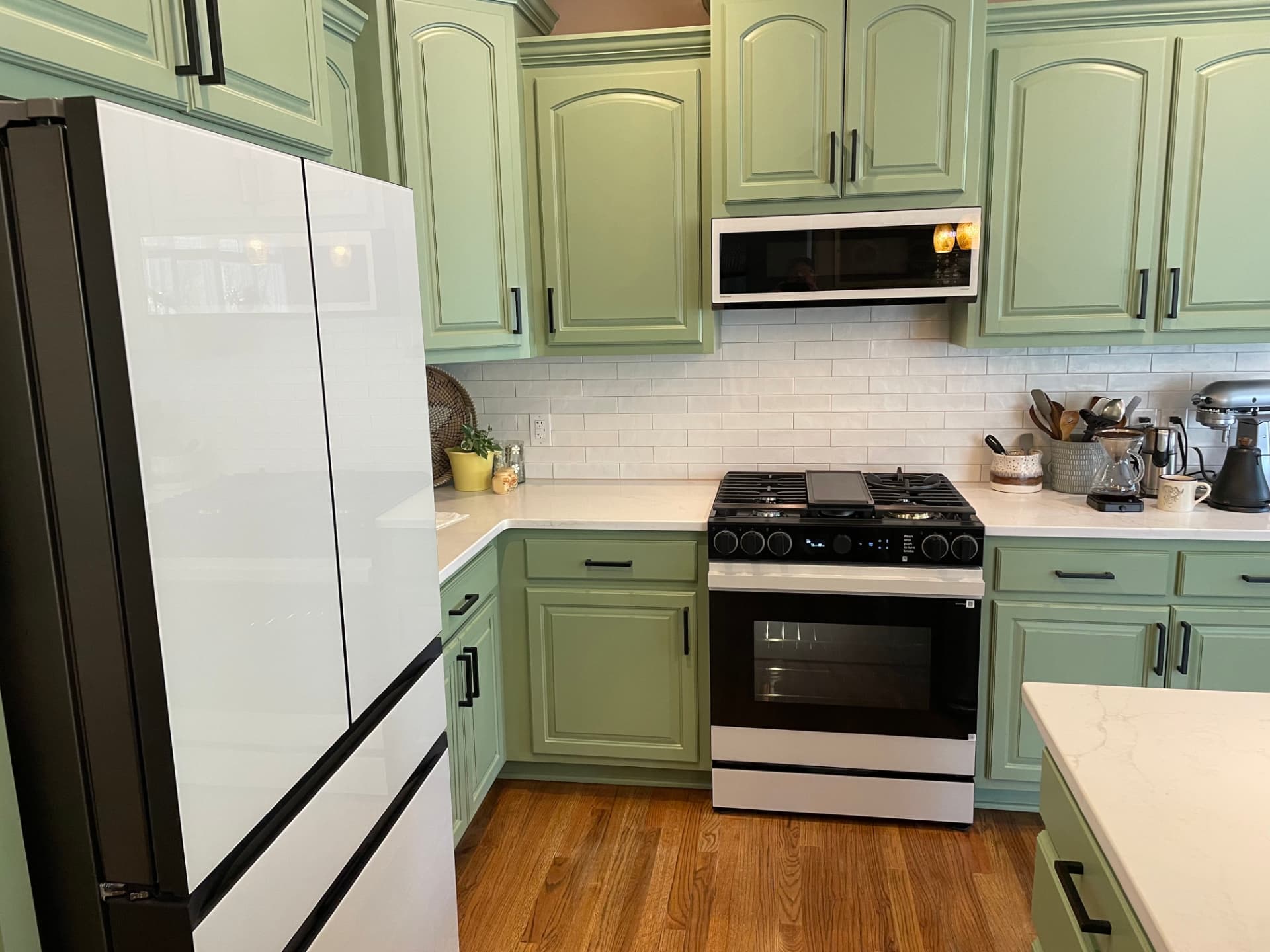 Kitchen cabinets repainted in soft sage green with black hardware and white subway tile